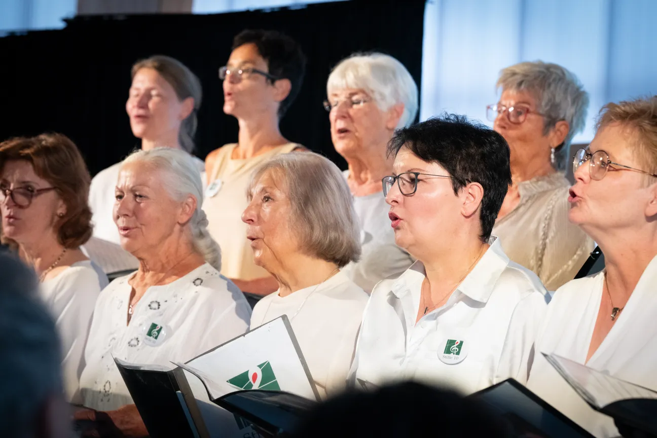 Frauen singen im Chor. Sie halten ein Liedbuch in der Hand.