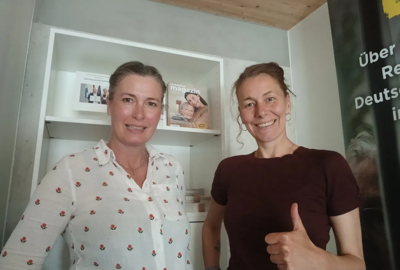 Zwei Frauen stehen lächelnd nebeneinander. Eine hält den Daumen hoch.