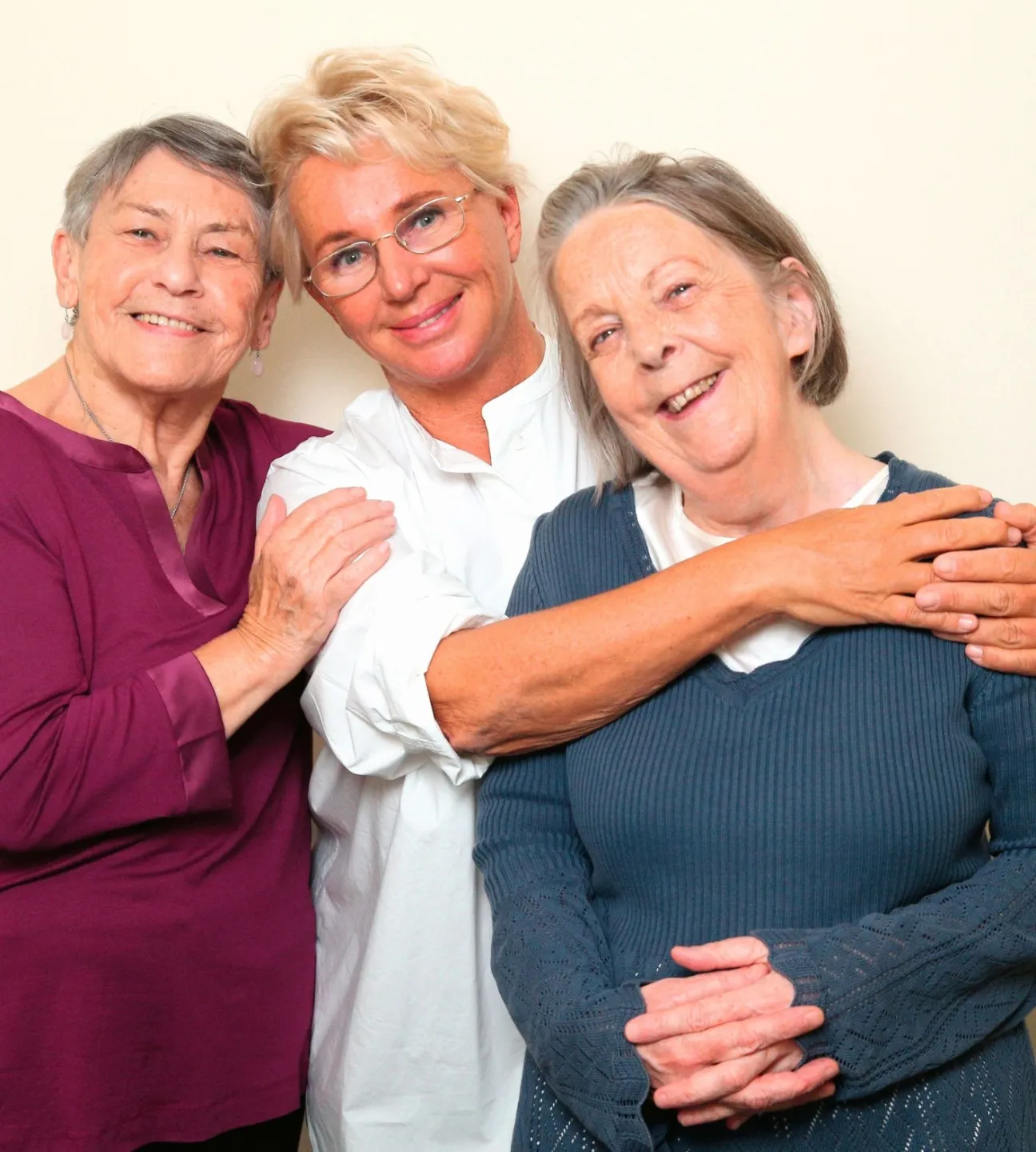 Drei Frauen unterschiedlichen Alters liegen sich freundlich lächelnd in den Armen.