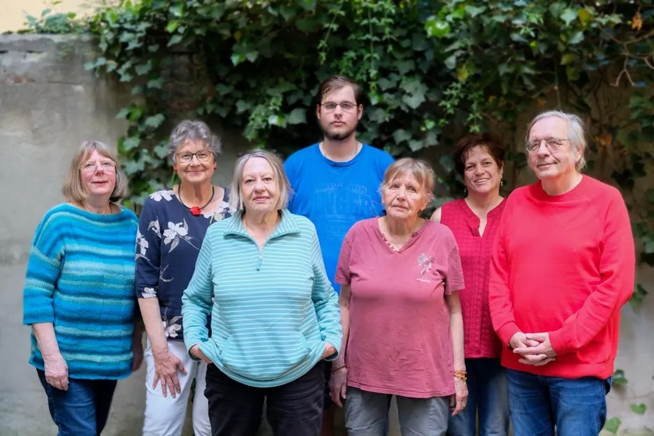 Ein jüngerer und mehrere ältere Menschen stehen in einer Gruppe schauen lächelnd nach vorn.